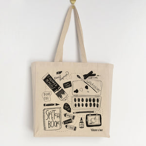 An eco-friendly canvas tote bag featuring playful hand-drawn illustrations of art supplies such as watercolor paints, pencils, and other creative tools. The bag is made from 12oz heavy weight cotton canvas with a gusseted edge, providing extra room and allowing it to stand upright when set down. The design is monochromatic, with black illustrations on a natural canvas background. The tote is locally and responsibly made in partnership with a printer in Denver, Colorado.